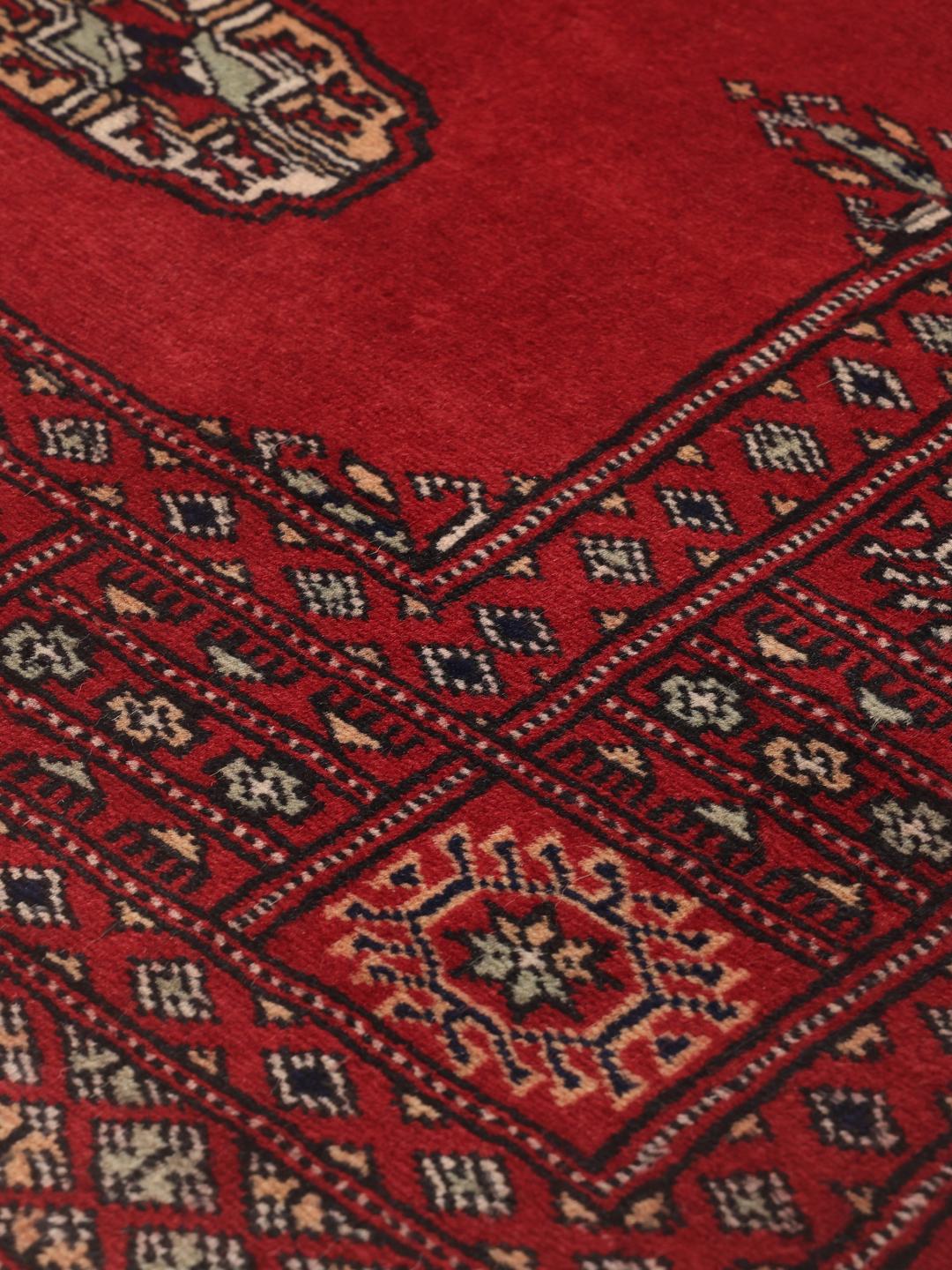 Hand-knotted Pakistan Bokhara rug in a deep red color with traditional motifs.