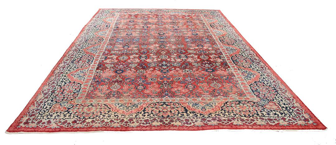 A large rectangular antique Sarouk rug from the Middle East featuring a vibrant red and dark-blue floral pattern