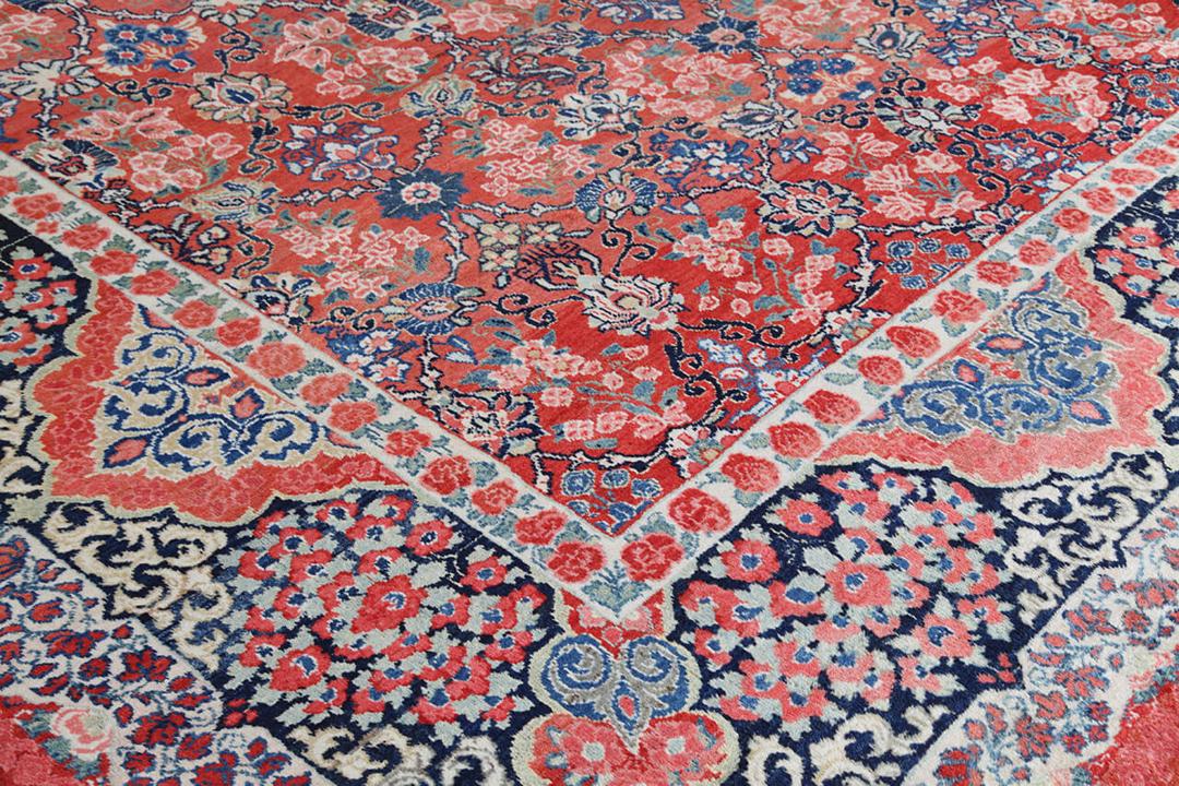 A large rectangular antique Sarouk rug from the Middle East featuring a vibrant red and dark-blue floral pattern