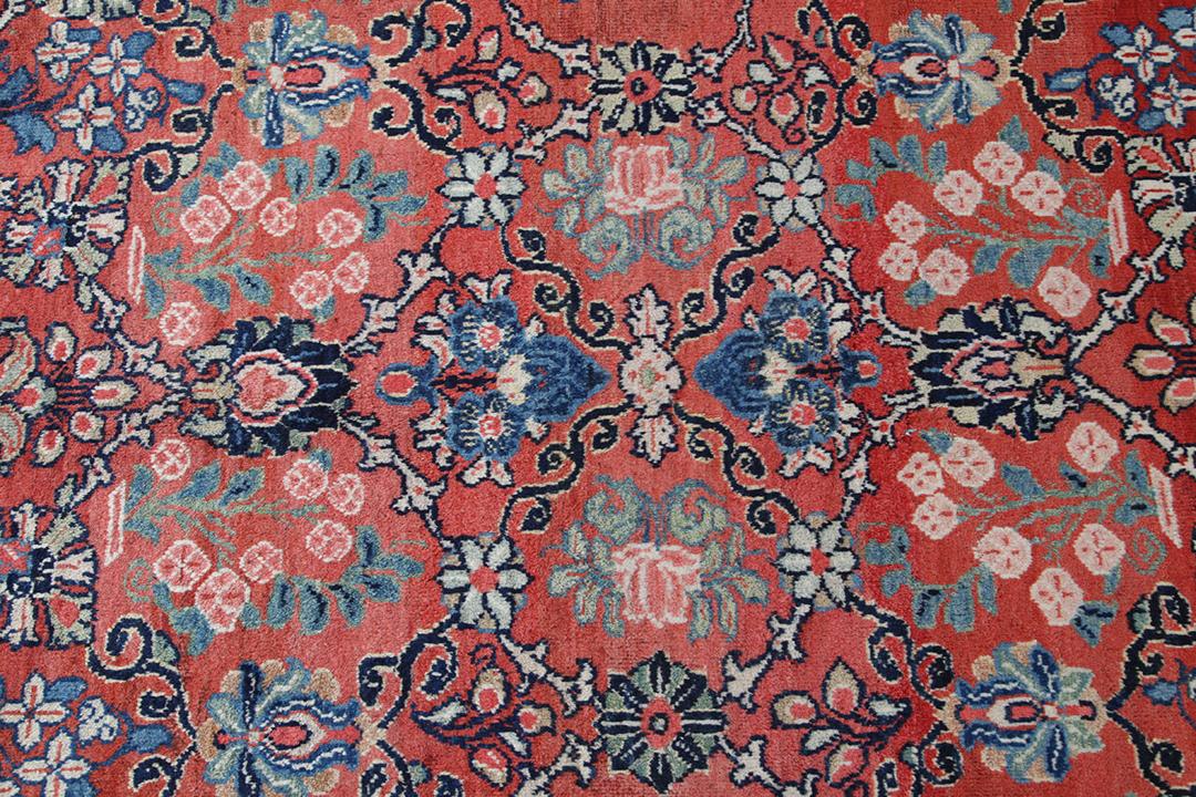 A large rectangular antique Sarouk rug from the Middle East featuring a vibrant red and dark-blue floral pattern