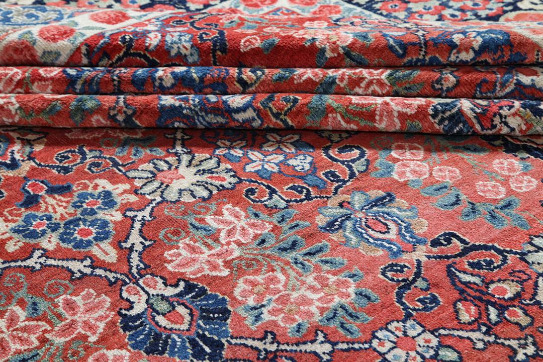 A large rectangular antique Sarouk rug from the Middle East featuring a vibrant red and dark-blue floral pattern