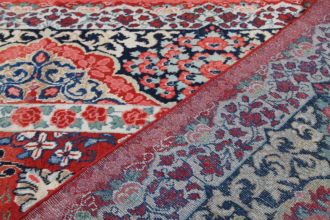 A large rectangular antique Sarouk rug from the Middle East featuring a vibrant red and dark-blue floral pattern