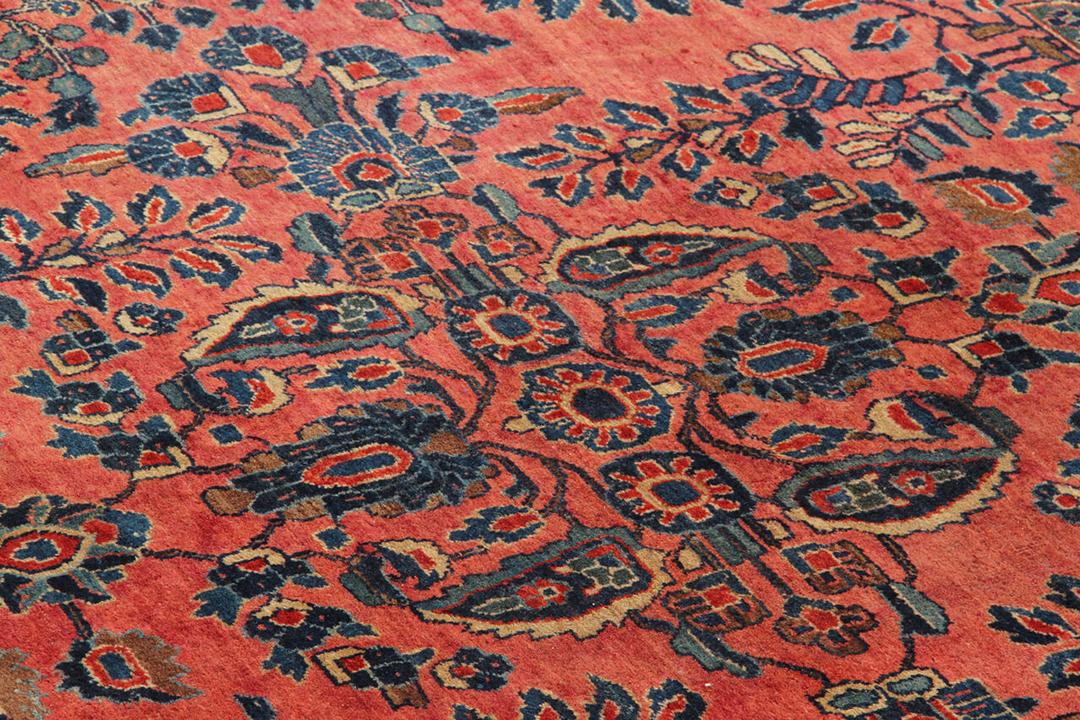 A large, rectangular antique Sarouk rug from the Middle East featuring a vibrant red field with intricate floral patterns and a dark border.