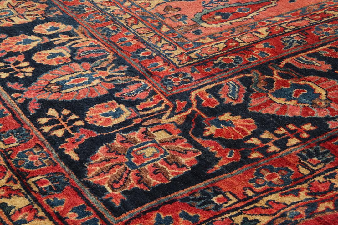 A large, rectangular antique Sarouk rug from the Middle East featuring a vibrant red field with intricate floral patterns and a dark border.