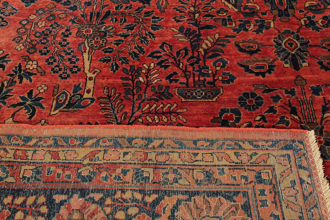 A large, rectangular antique Sarouk rug from the Middle East featuring a vibrant red field with intricate floral patterns and a dark border.