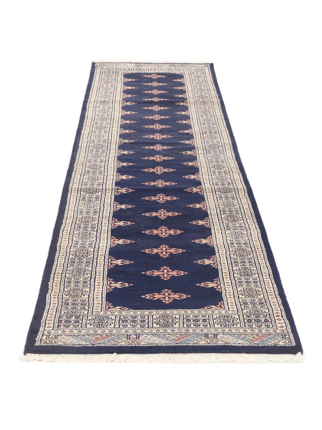 A long, narrow hand-knotted runner from Pakistan with a deep blue field and repeating motifs.