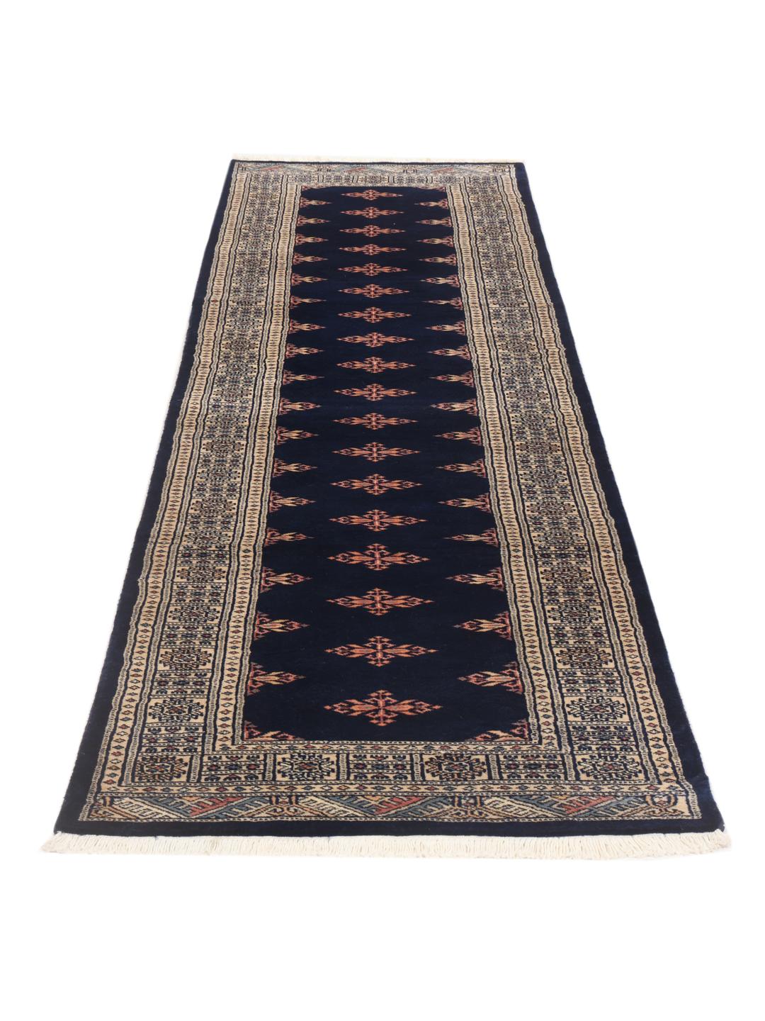 A long, narrow hand-knotted runner from Pakistan with a deep blue field and repeating motifs.