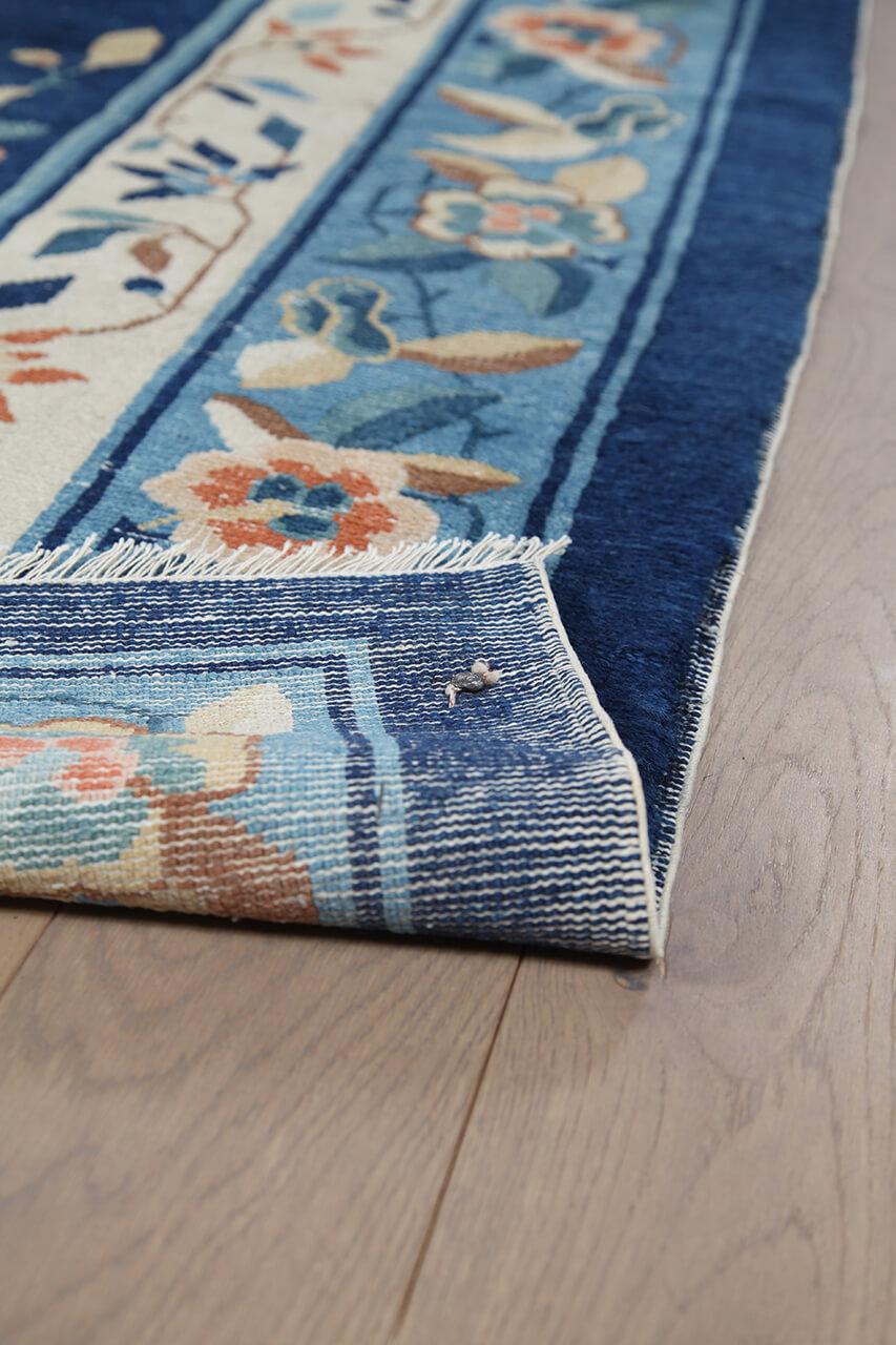 Antikt kinesisk tæppe med blomstermotiver og et dybblåt felt