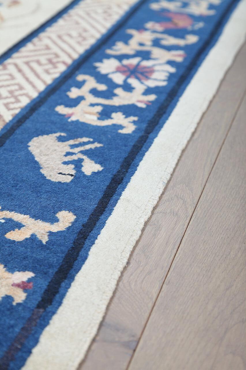 Antikt kinesisk tæppe med traditionelle motiver på en beige bund og blå bort