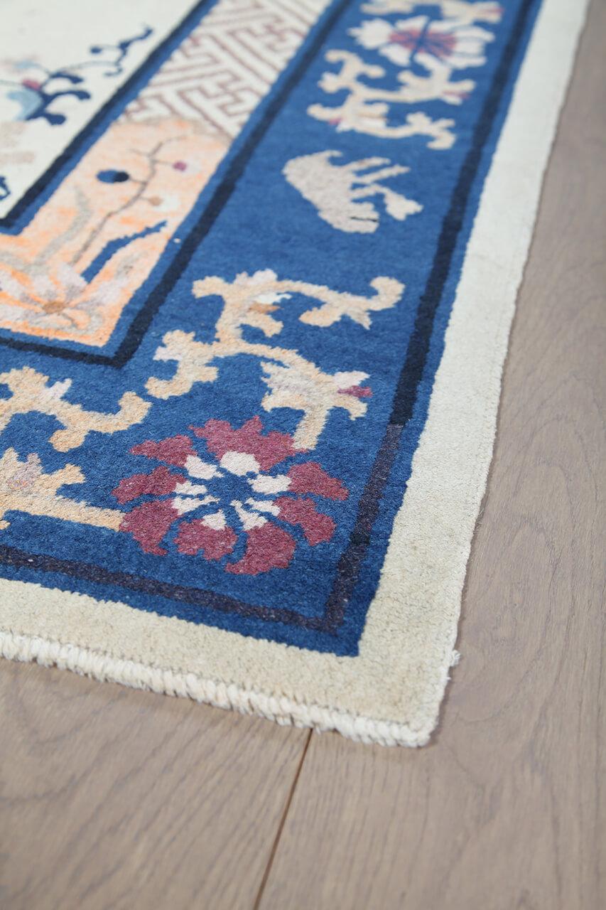 Antikt kinesisk tæppe med traditionelle motiver på en beige bund og blå bort