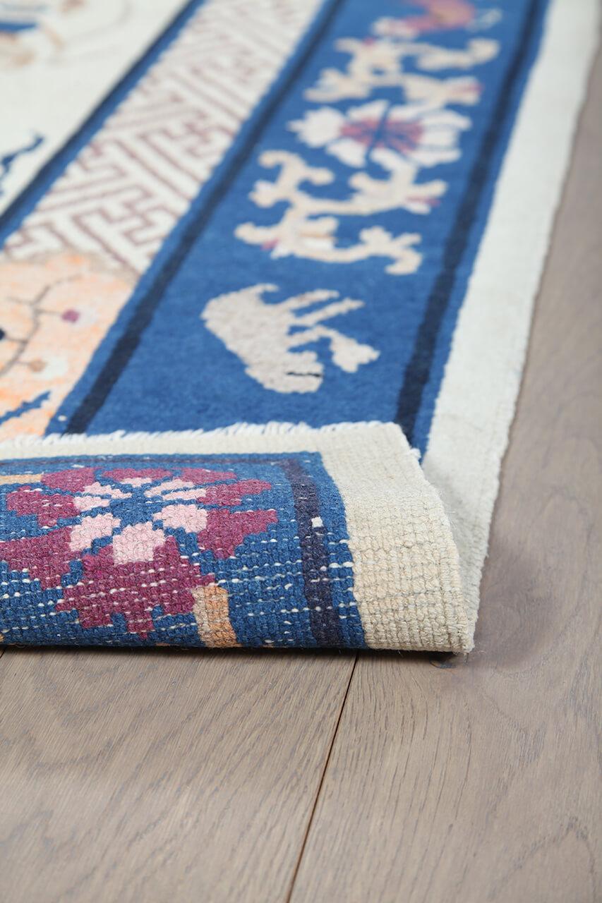 Antikt kinesisk tæppe med traditionelle motiver på en beige bund og blå bort