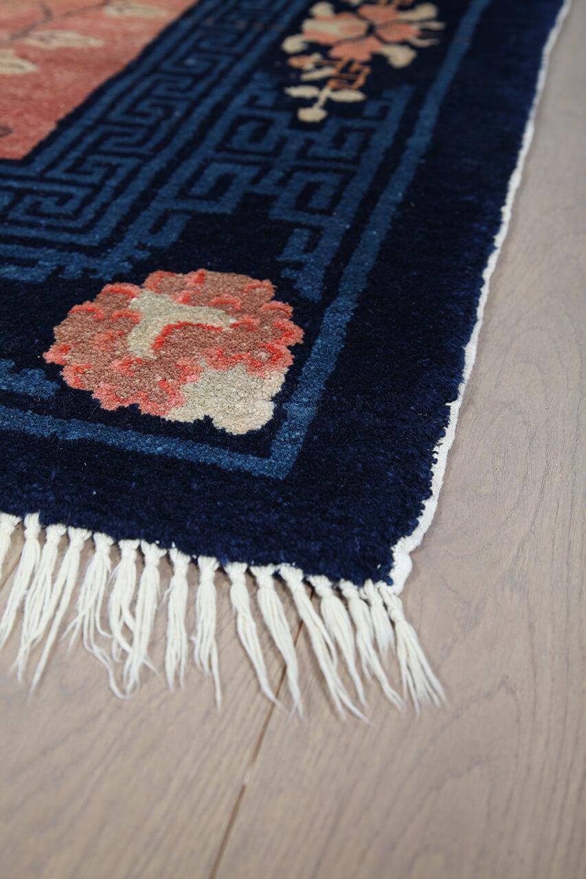 Een prachtig antiek tapijt uit China met een rood veld en bloempatronen.