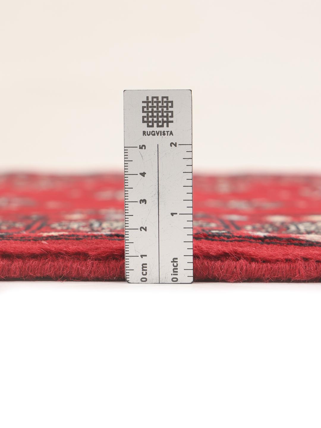 A hand-knotted Pakistan Bokhara rug with a deep red field and traditional geometric motifs.
