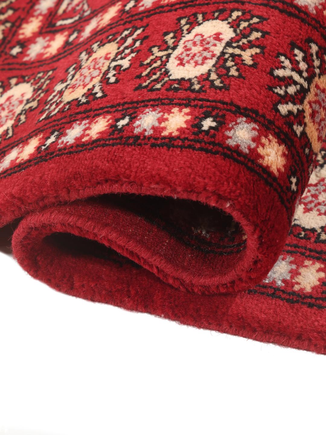 A hand-knotted Pakistan Bokhara rug with a deep red field and traditional geometric motifs.