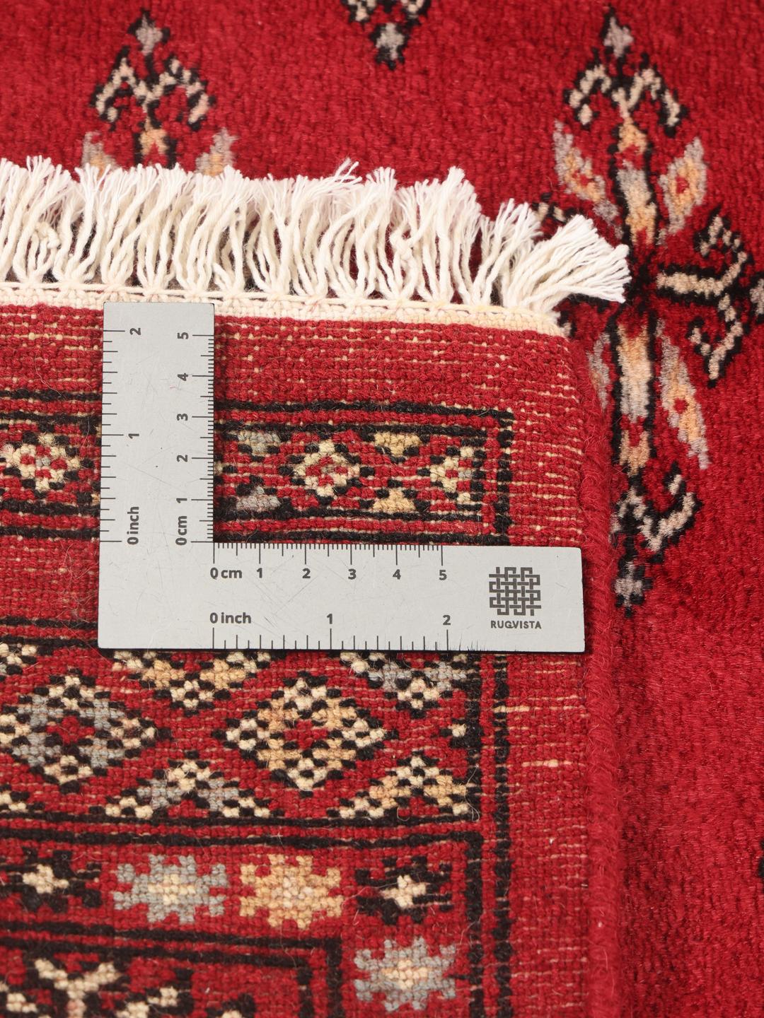 A hand-knotted Pakistan Bokhara rug with a deep red field and traditional geometric motifs.