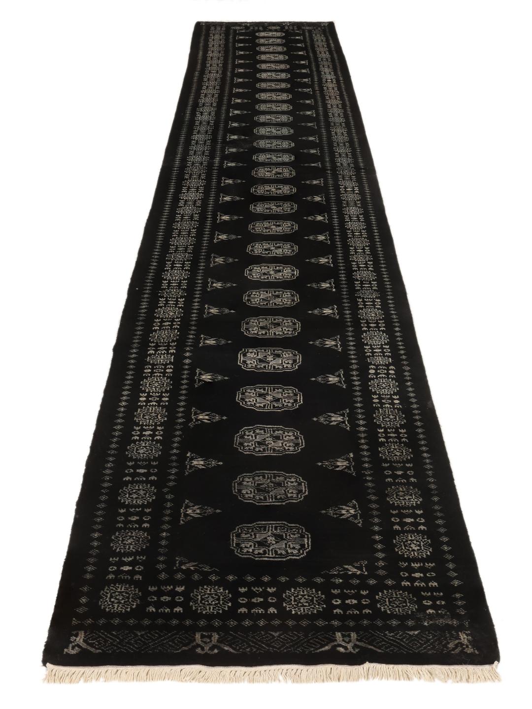 Un long tapis couloir noué à la main, de couleur noire, originaire du Pakistan avec des motifs répétitifs traditionnels.