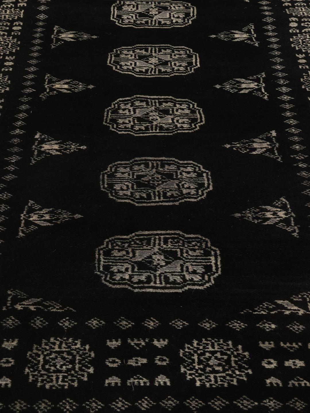 Un long tapis couloir noué à la main, de couleur noire, originaire du Pakistan avec des motifs répétitifs traditionnels.
