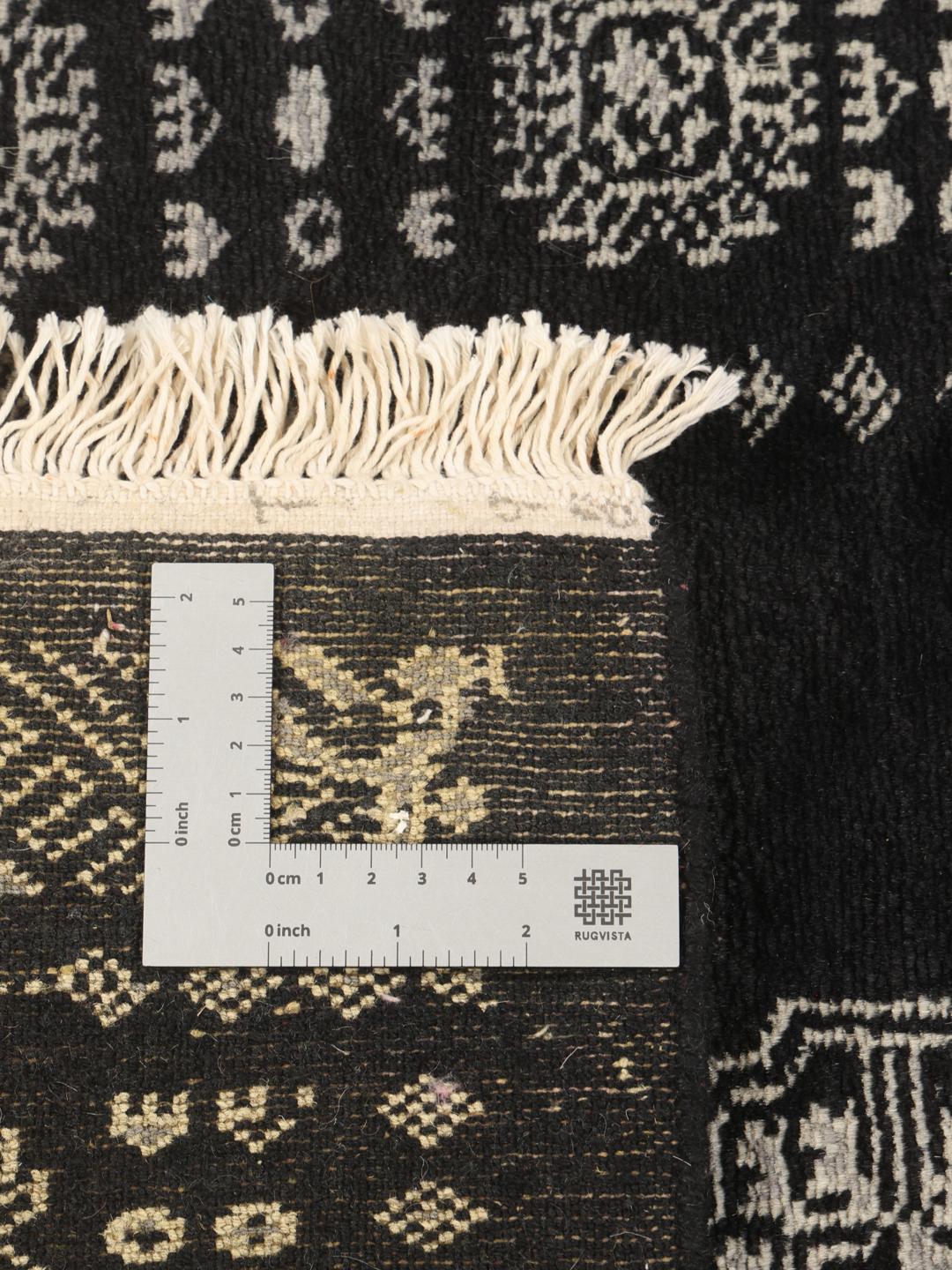 Un long tapis couloir noué à la main, de couleur noire, originaire du Pakistan avec des motifs répétitifs traditionnels.