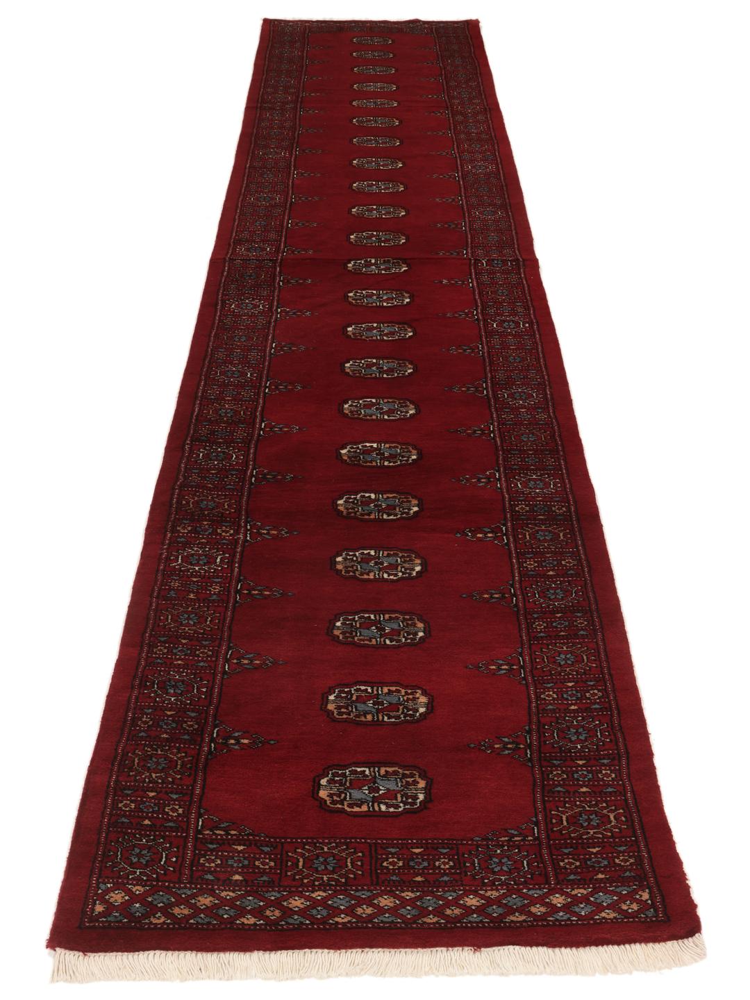A long, hand-knotted Pakistan Bokhara runner in dark-red with repeating medallion patterns.