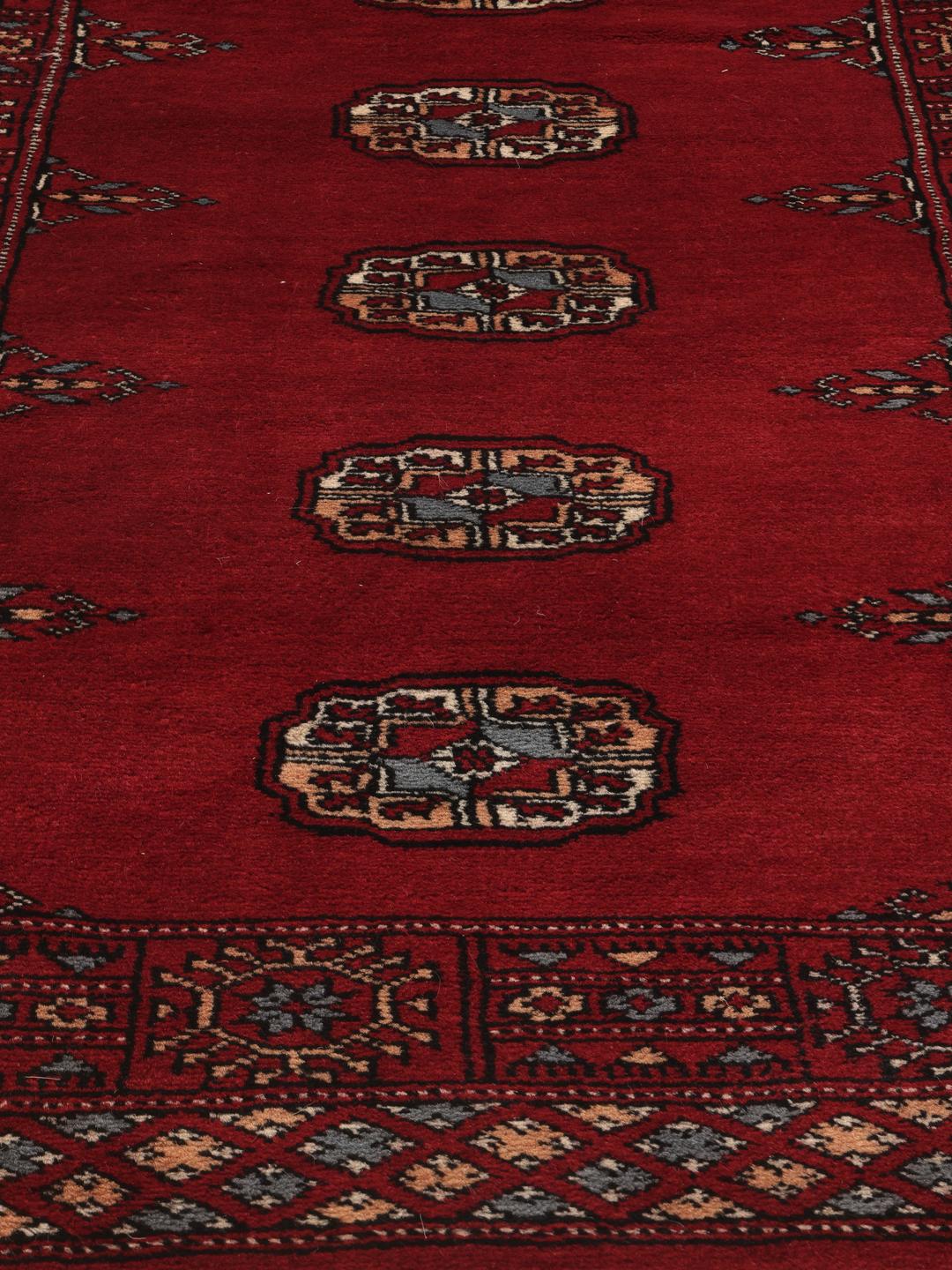 A long, hand-knotted Pakistan Bokhara runner in dark-red with repeating medallion patterns.