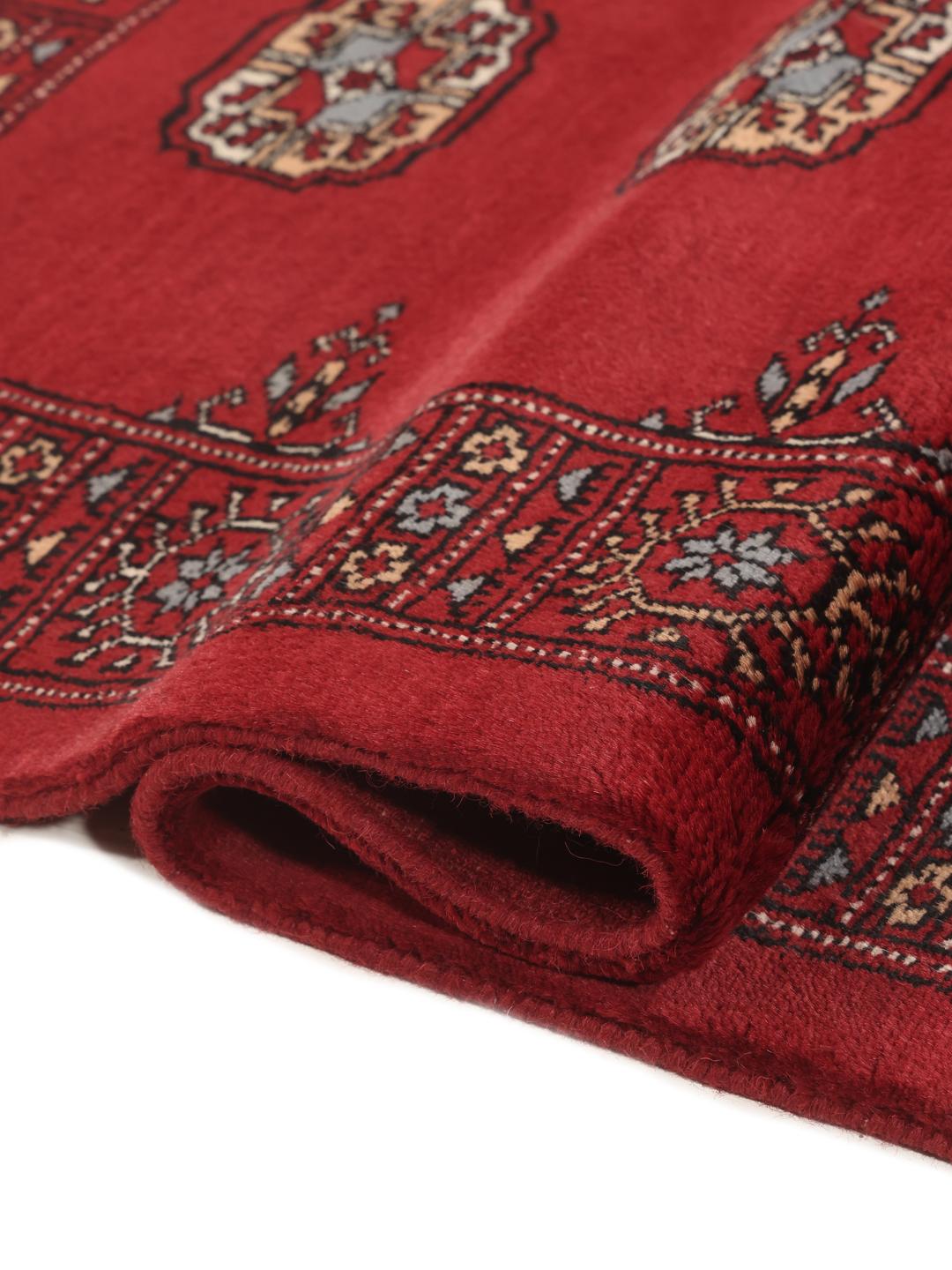A long, hand-knotted Pakistan Bokhara runner in dark-red with repeating medallion patterns.
