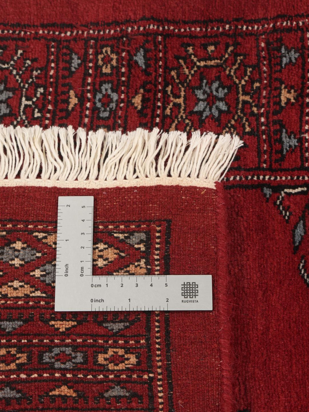 A long, hand-knotted Pakistan Bokhara runner in dark-red with repeating medallion patterns.