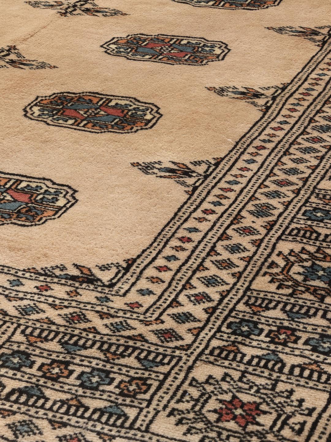 A hand-knotted Pakistan Bokhara rug with a beige field and traditional geometric motifs.