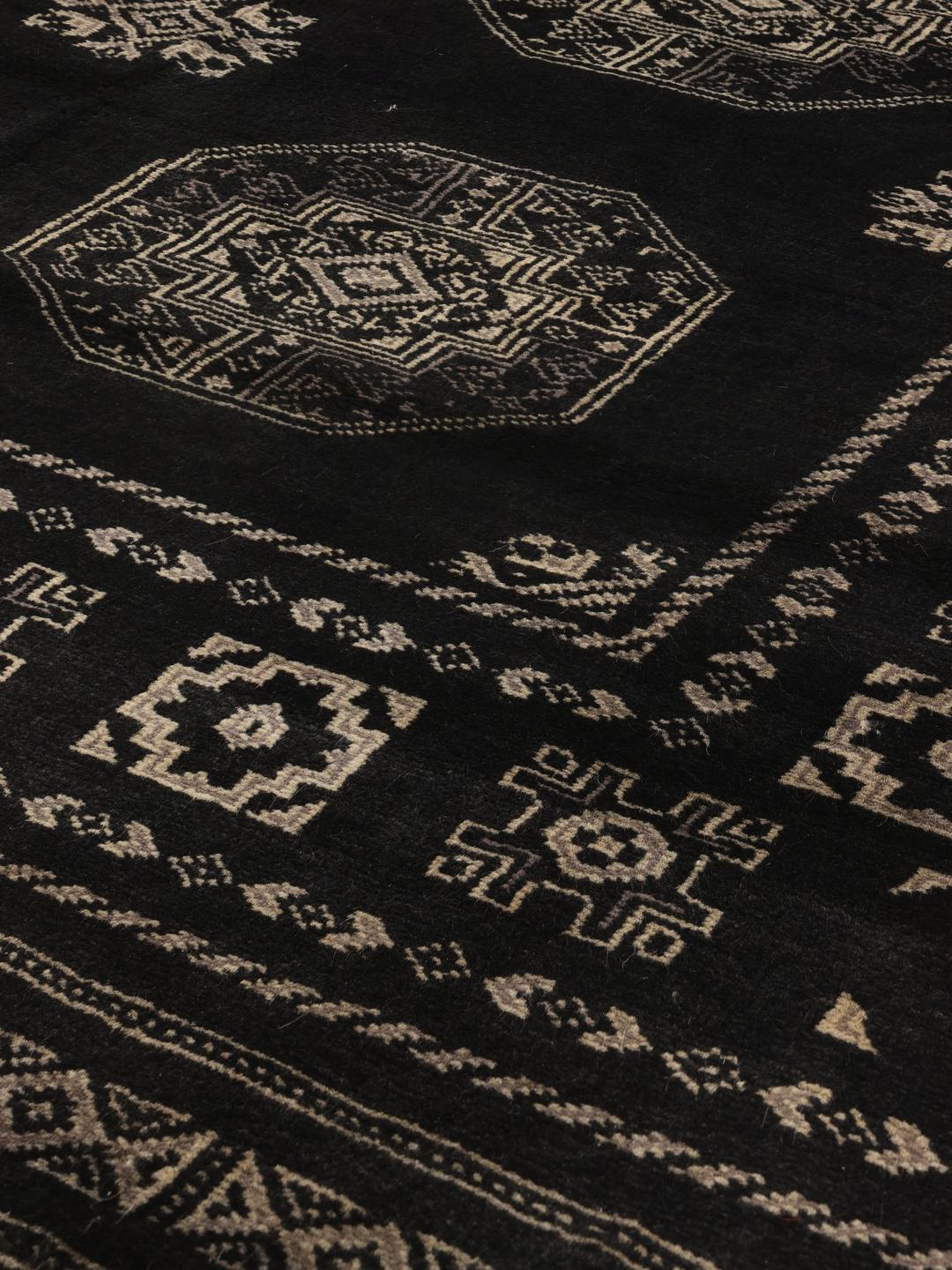 A hand-knotted Pakistan Bokhara rug with a dark field and geometric motifs.