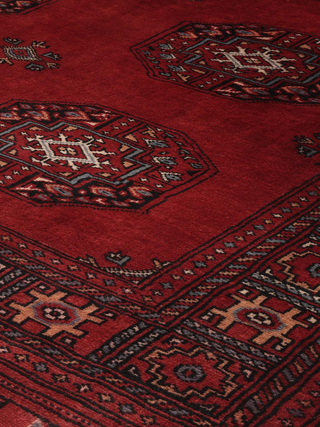 A hand-knotted Pakistan Bokhara rug in deep red with traditional gul motifs.