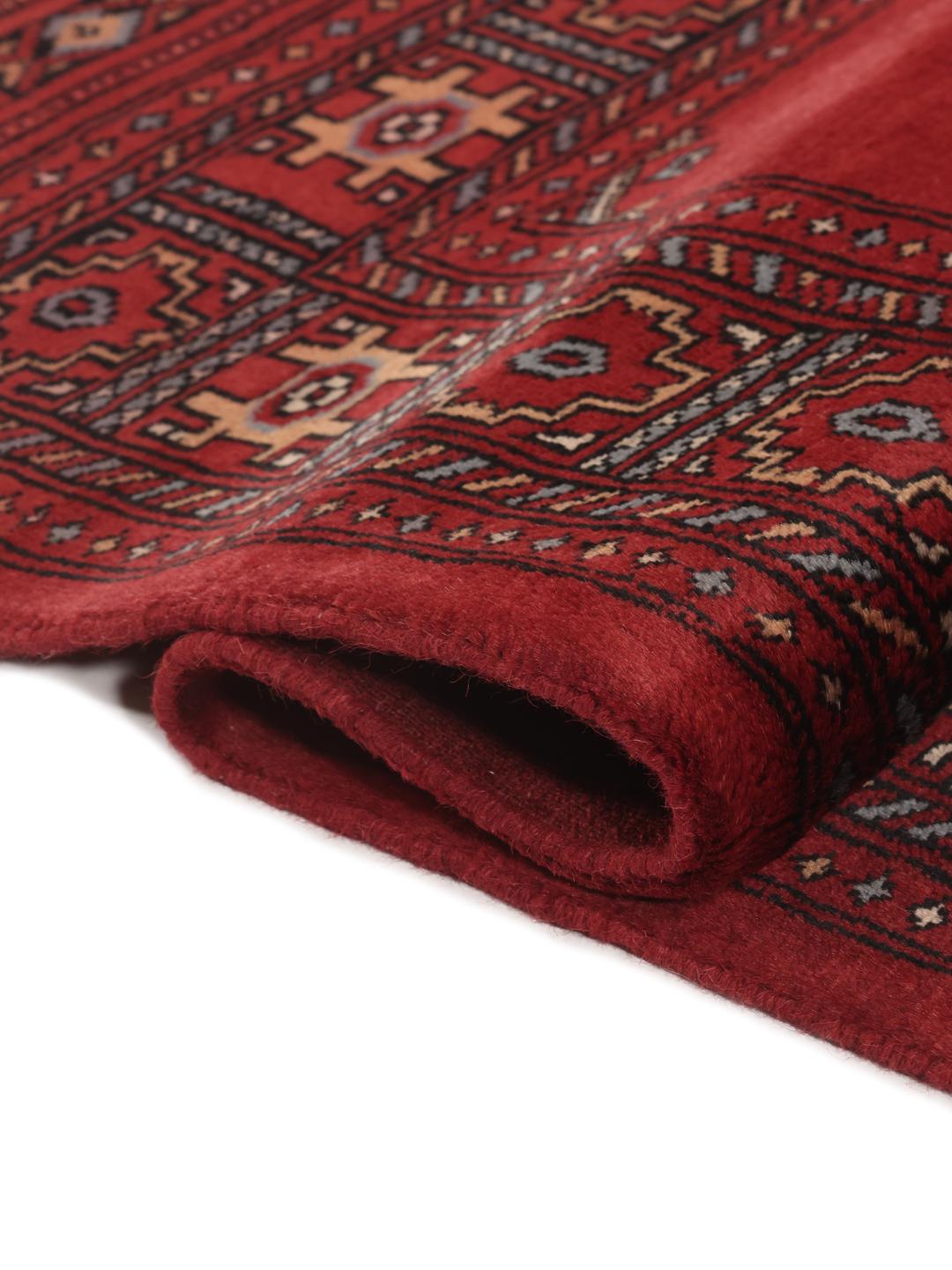 A hand-knotted Pakistan Bokhara rug in deep red with traditional gul motifs.