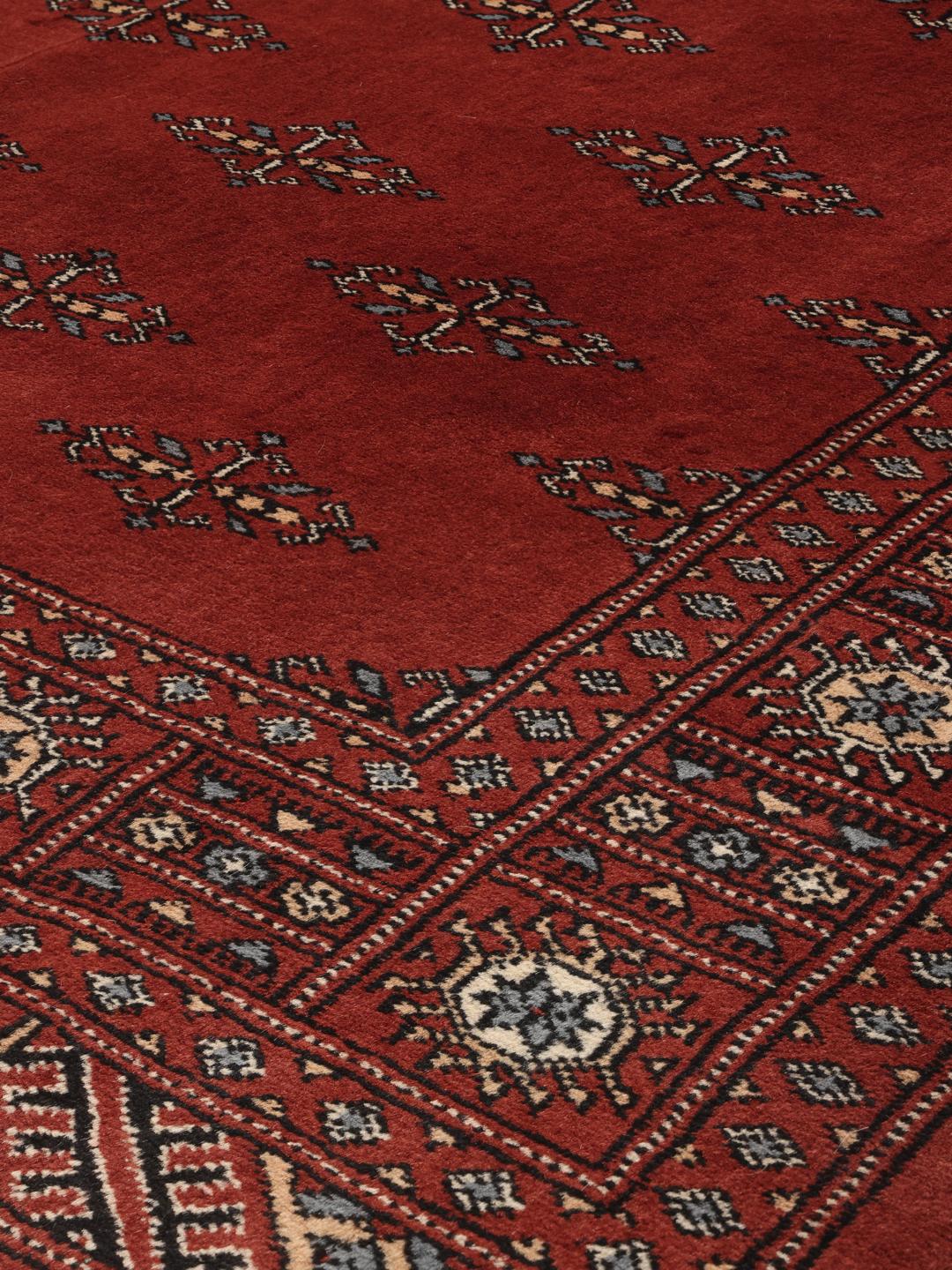 A hand-knotted Pakistan Bokhara rug in deep red with repeating geometric motifs.