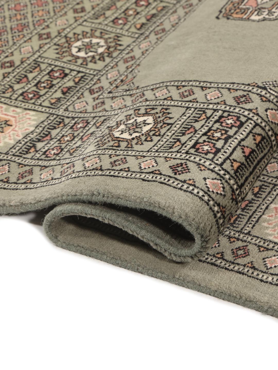 A hand-knotted Pakistan Bokhara 3ply rug with a sage green field and traditional motifs.