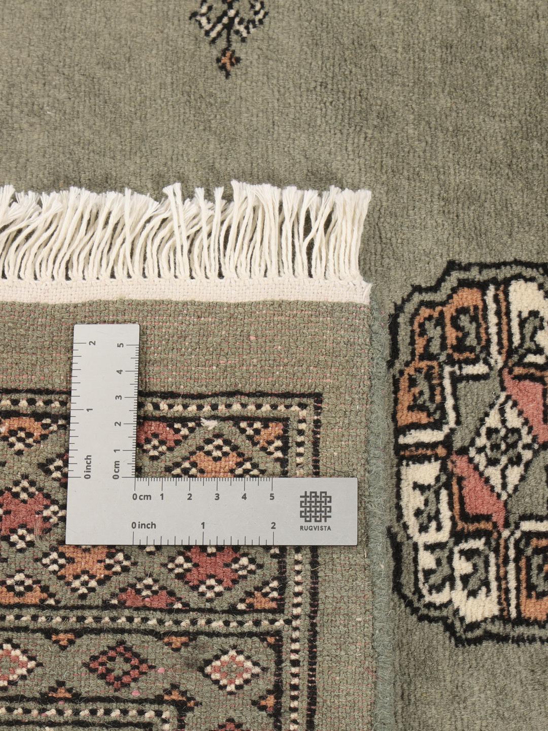 A hand-knotted Pakistan Bokhara 3ply rug with a sage green field and traditional motifs.