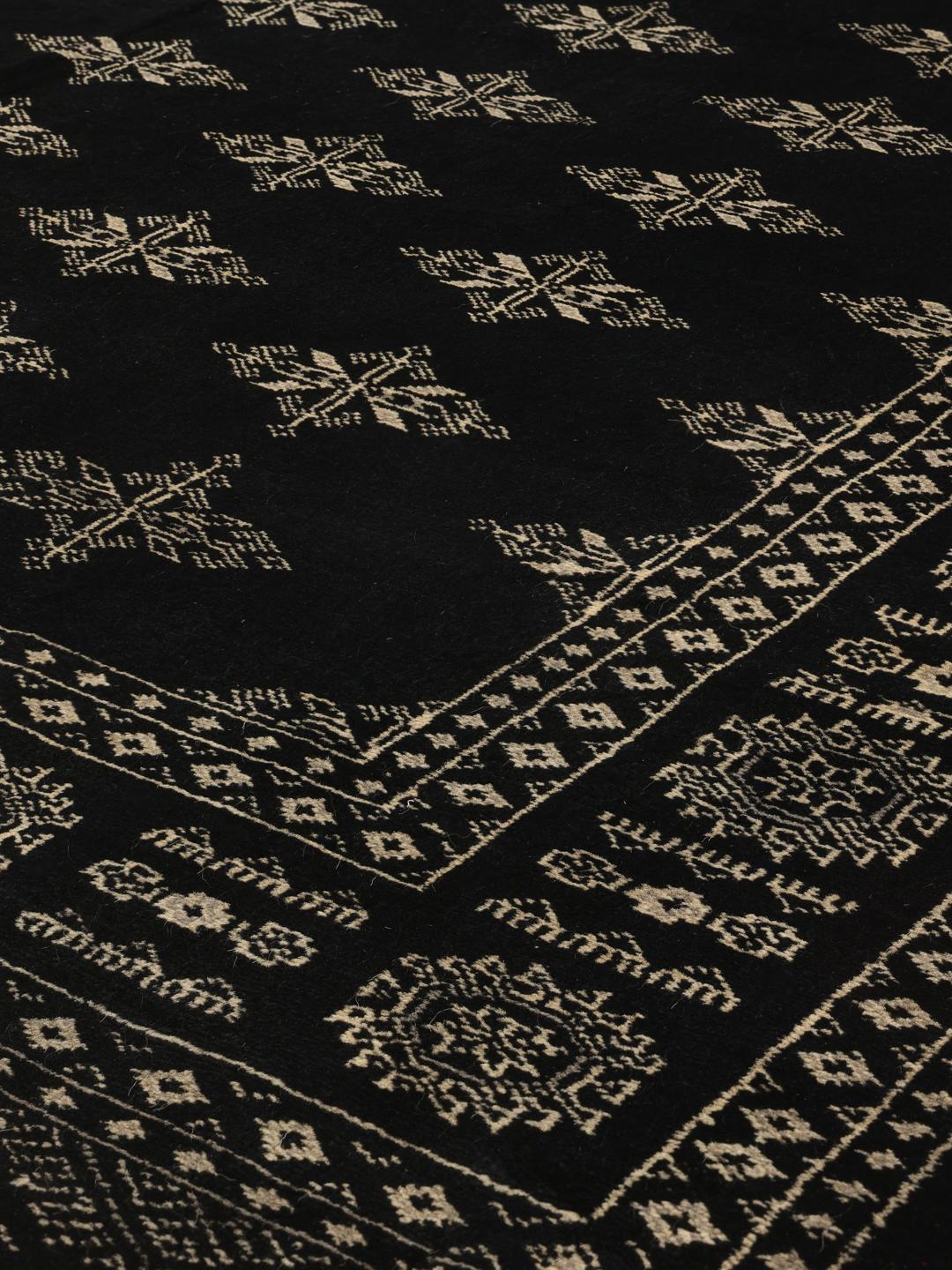 Een rechthoekig, met de hand geknoopt Pakistan Bokhara tapijt met een zwart veld en geometrische patronen.