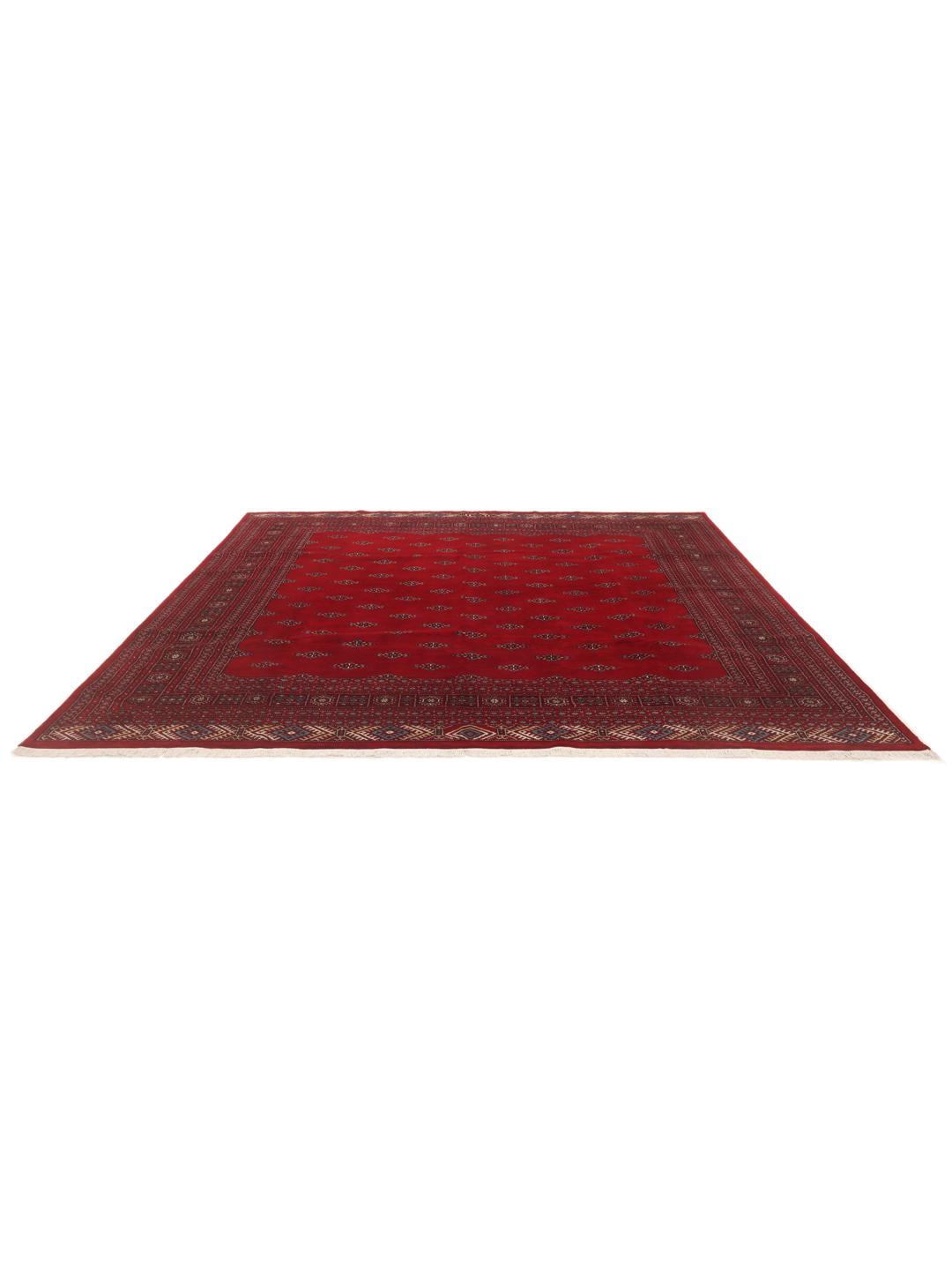 Een groot, vierkant Pakistan Bokhara vloerkleed met een dieprood veld en terugkerende geometrische motieven.