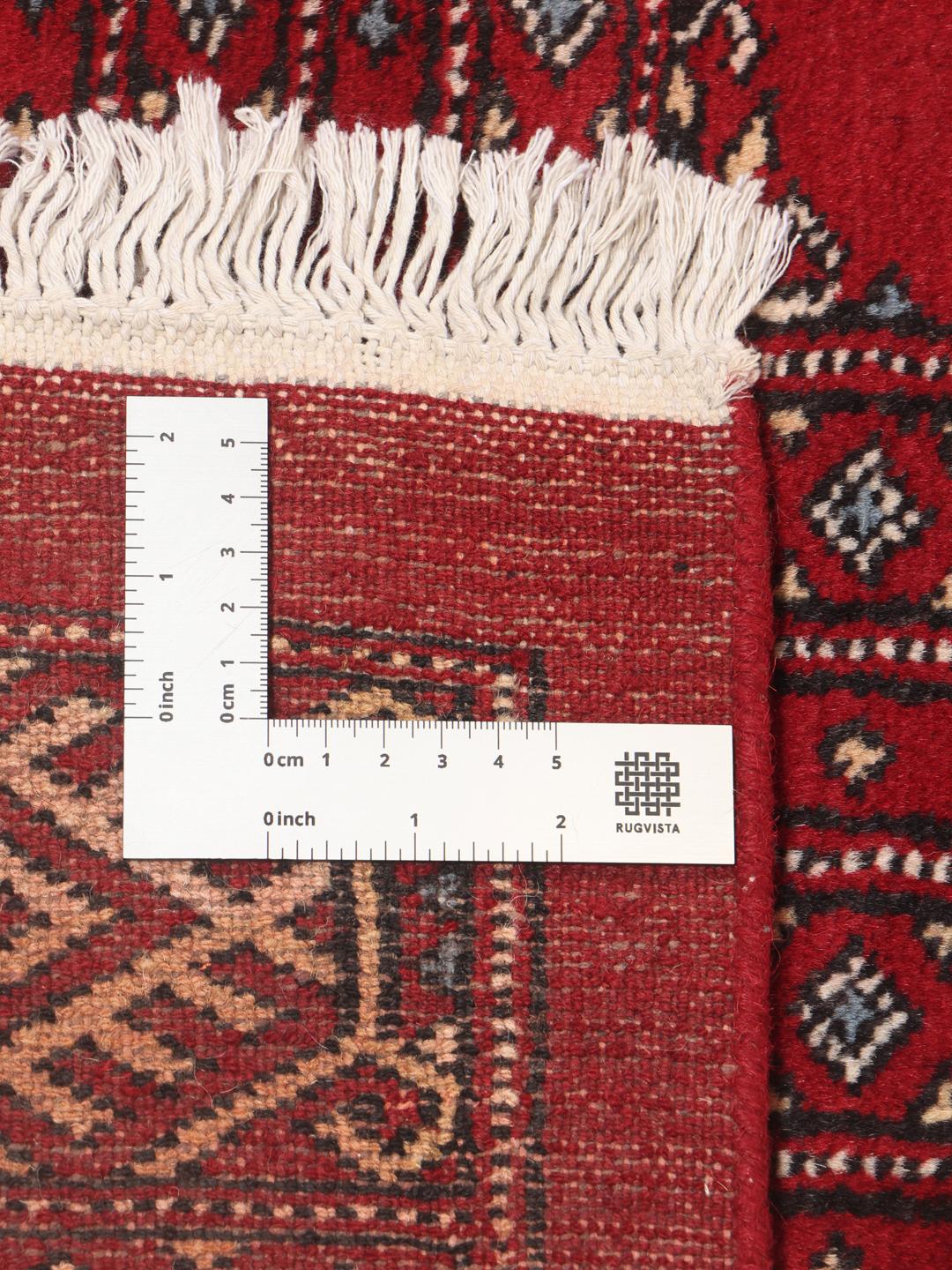 Een groot, vierkant Pakistan Bokhara vloerkleed met een dieprood veld en terugkerende geometrische motieven.