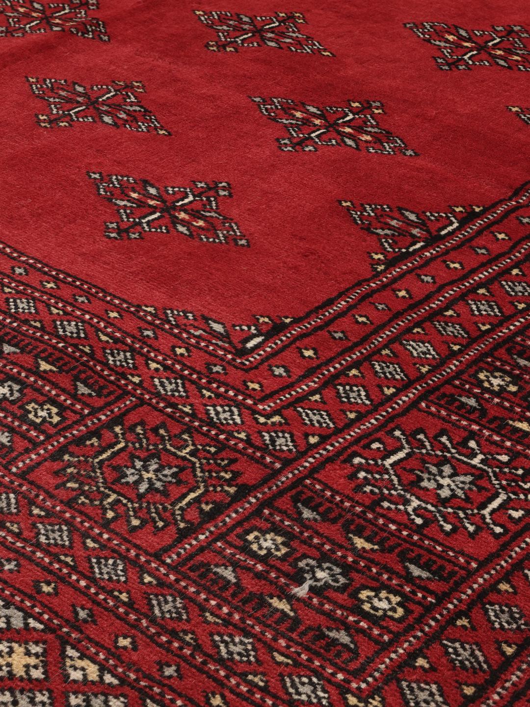 Ręcznie wiązany dywan pakistański z głębokim czerwonym tłem i powtarzającymi się geometrycznymi motywami