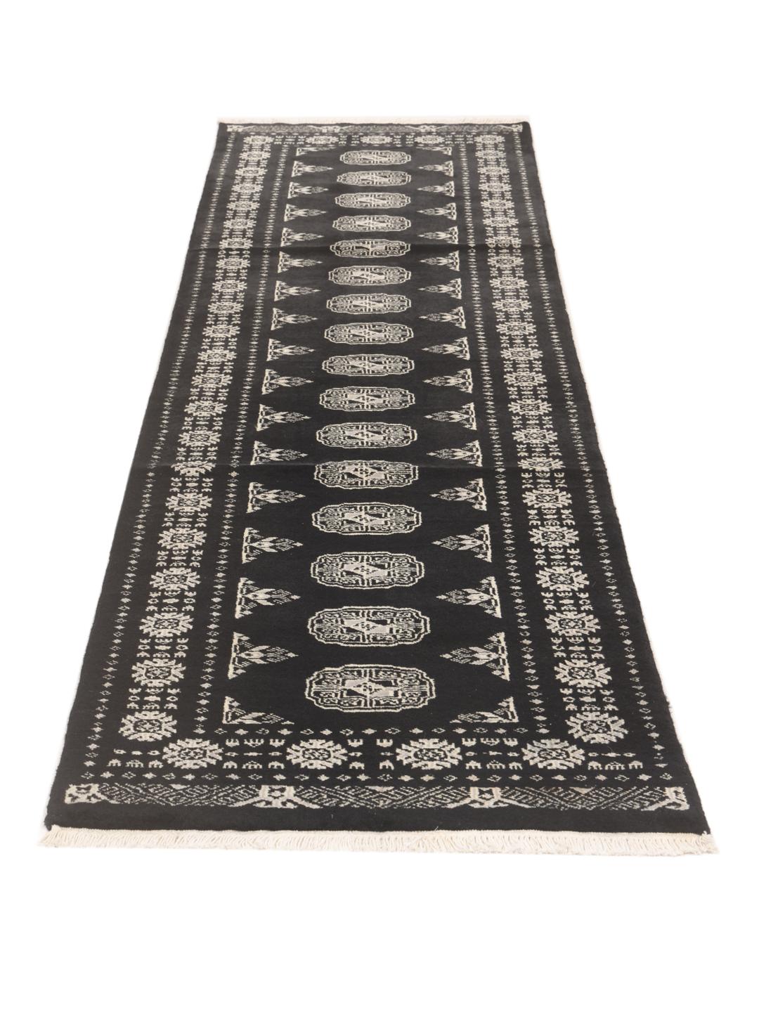 A long, hand-knotted runner from Pakistan with a black field and traditional patterns.
