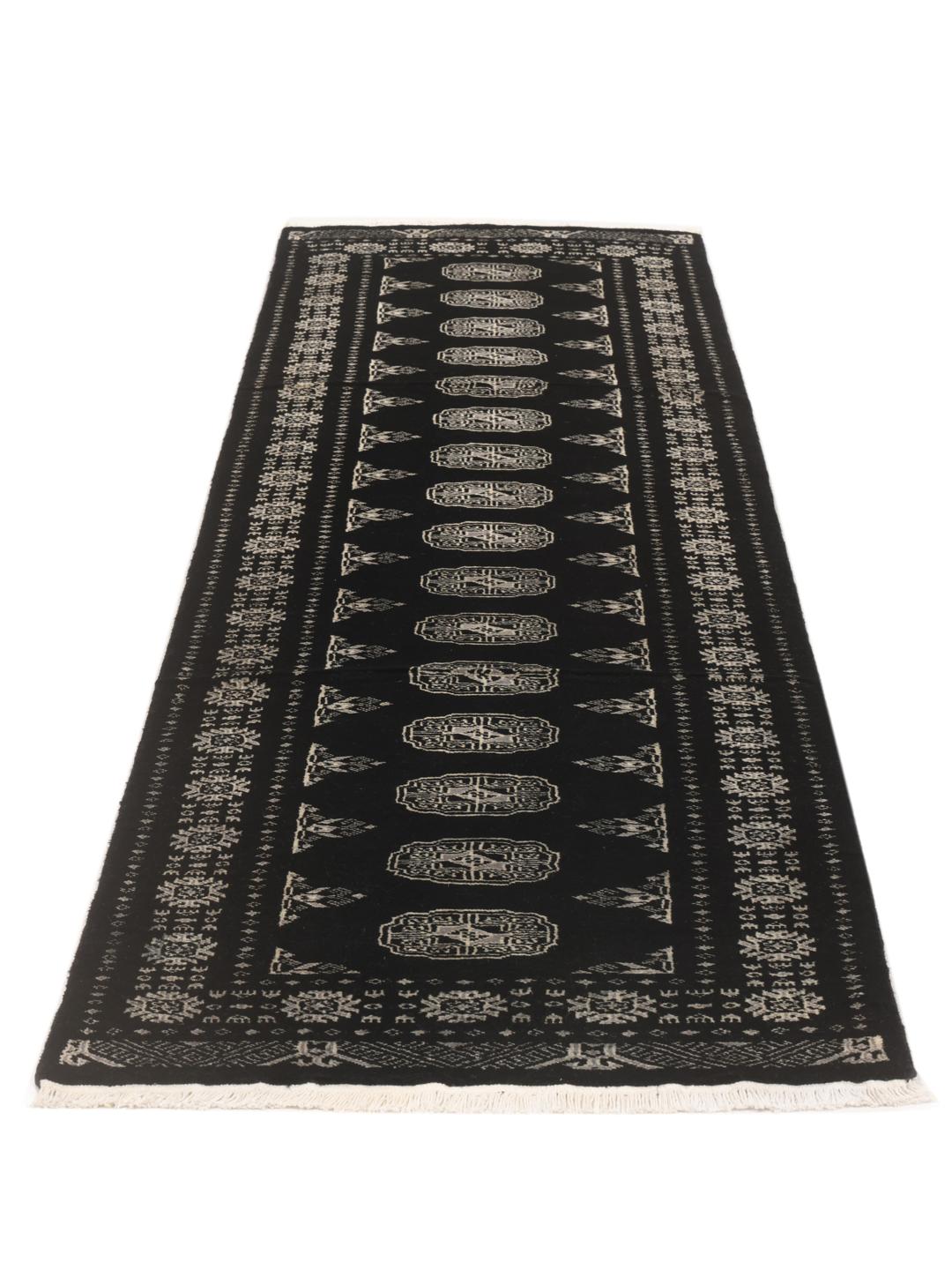 A long, hand-knotted runner from Pakistan with a black field and traditional patterns.