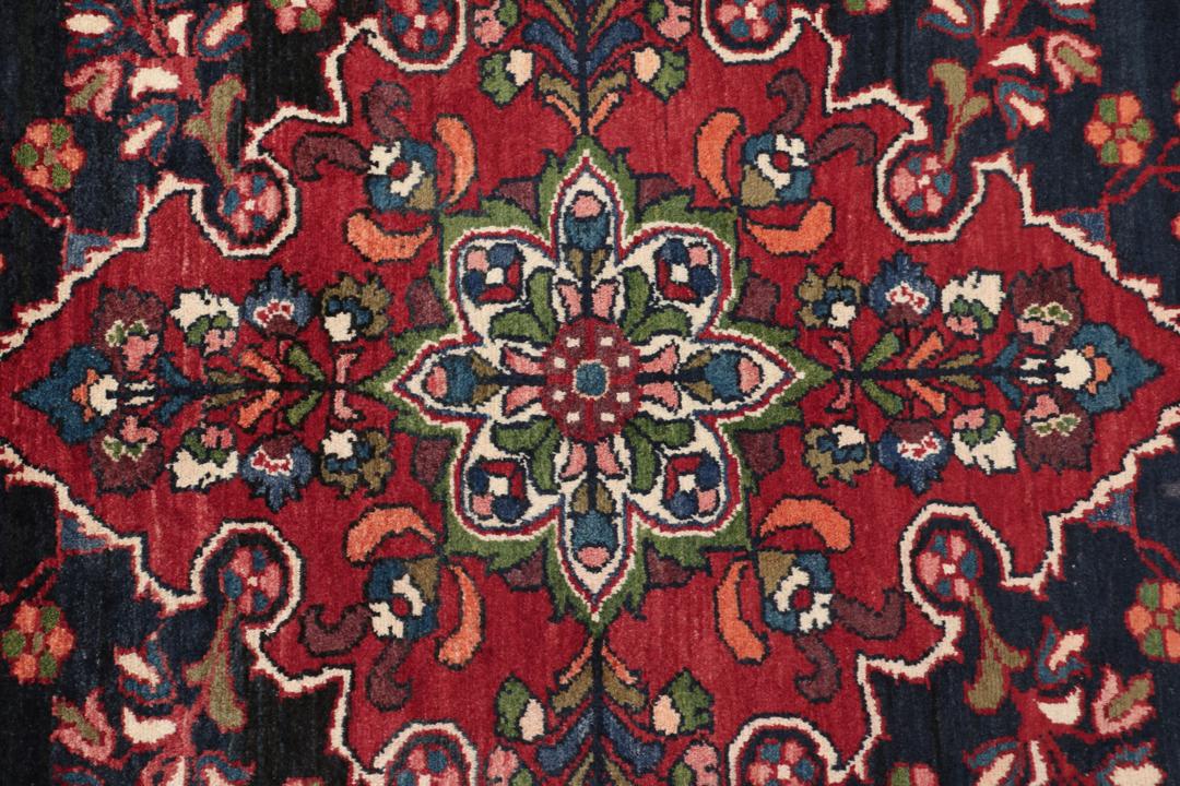 Een handgeknoopt Lillian-tapijt uit het Midden-Oosten met een donkerblauw veld en een centraal rood bloemenmedaillon.