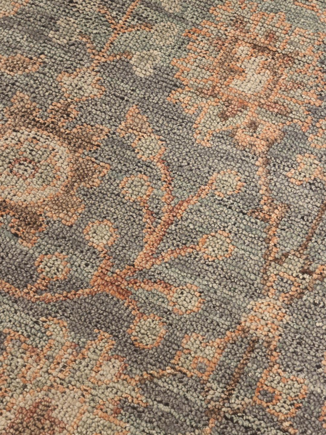 Een groot handgeknoopt Indiaas tapijt met een zacht blauw en perzikkleurig bloemenpatroon.