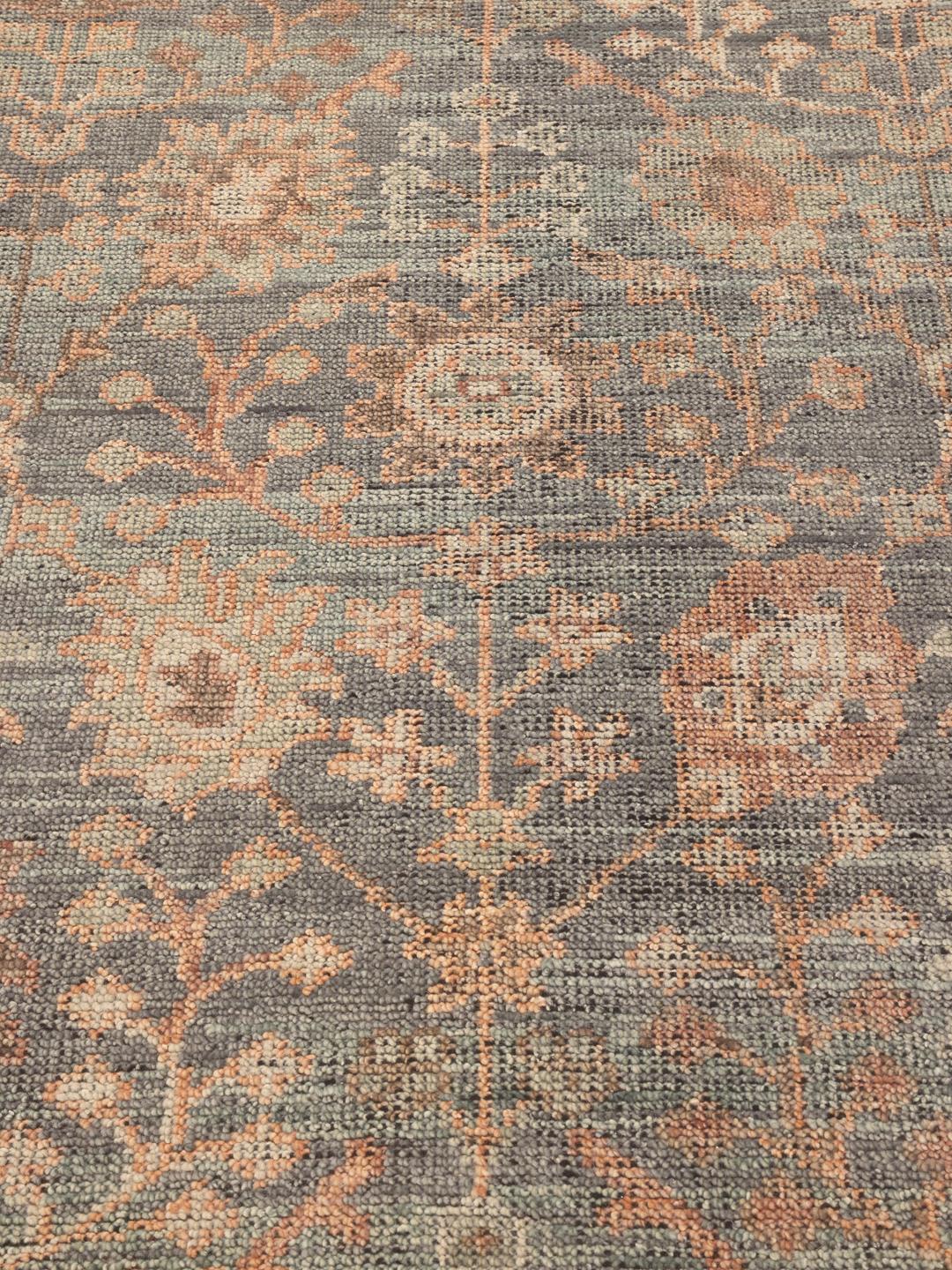 Een groot handgeknoopt Indiaas tapijt met een zacht blauw en perzikkleurig bloemenpatroon.