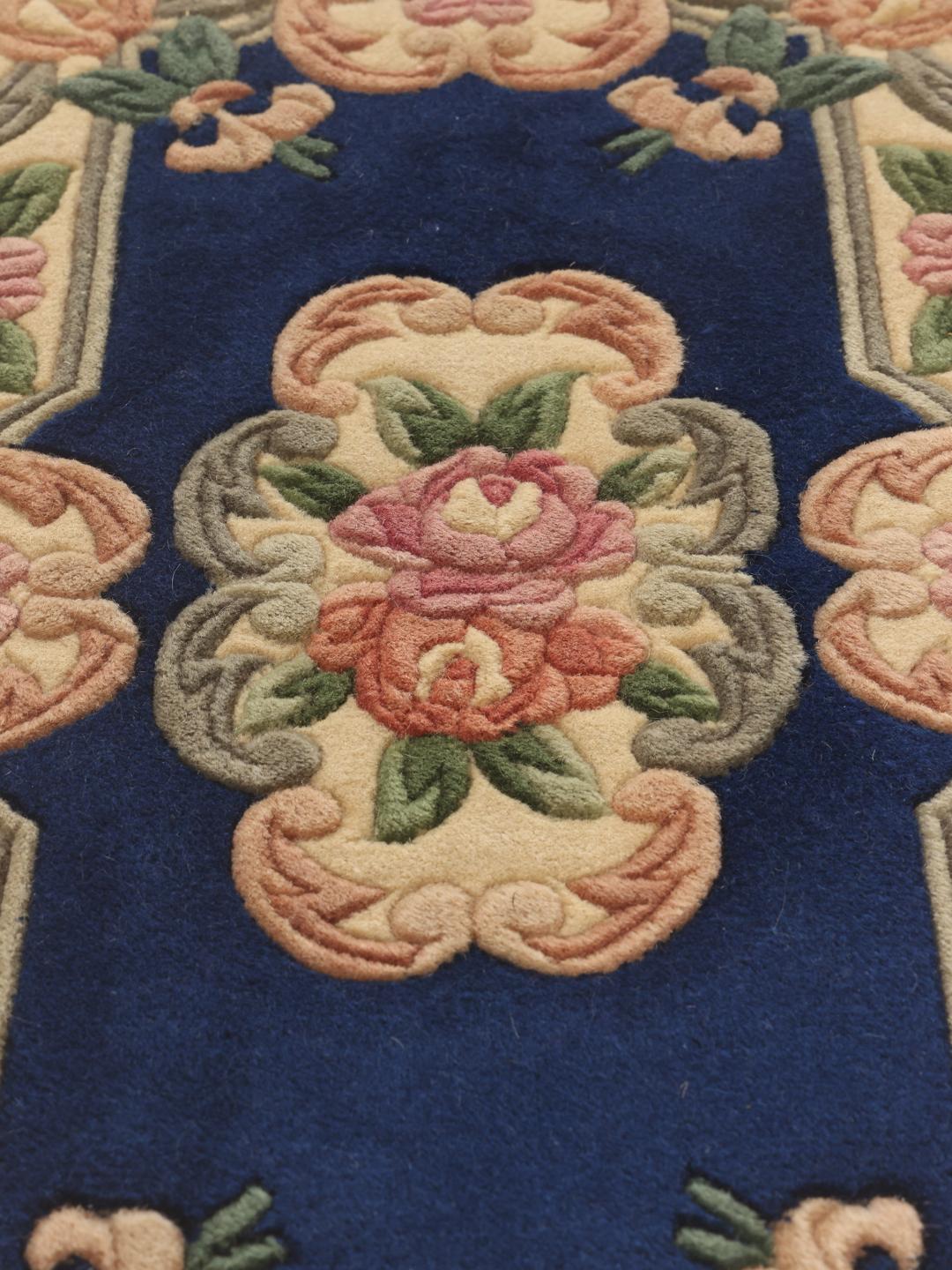 Et rektangulært håndlavet kinesisk tæppe med en dybblå bund og blomstermønster.