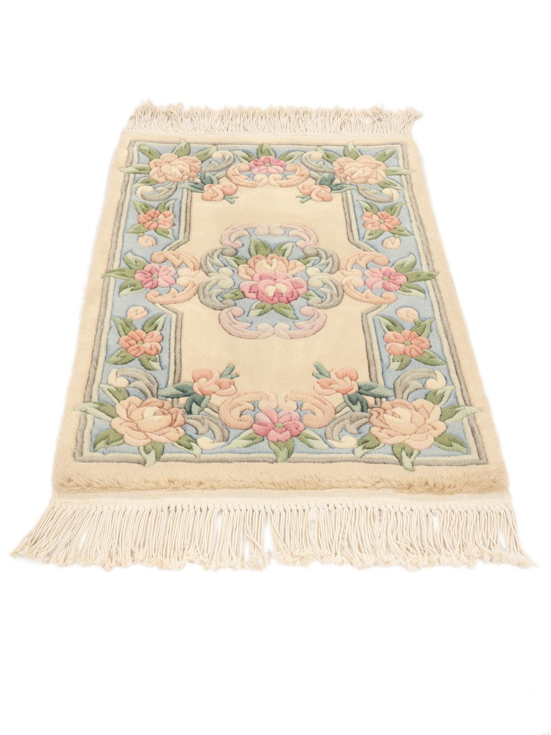 Et rektangulært tæppe fra Kina med blomstermønstre i beige, blå og lyserød.