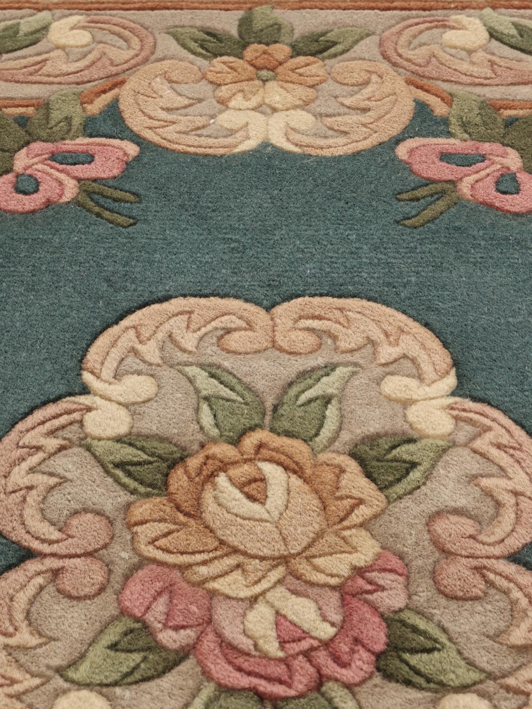 Et rektangulært kinesisk tæppe med blomstermønstre i nuancer af teal, lyserød og beige.
