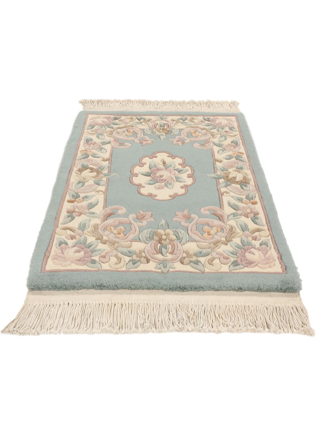 Et rektangulært håndknyttet tæppe fra Kina med et blomstermønster i lyseblå og beige.