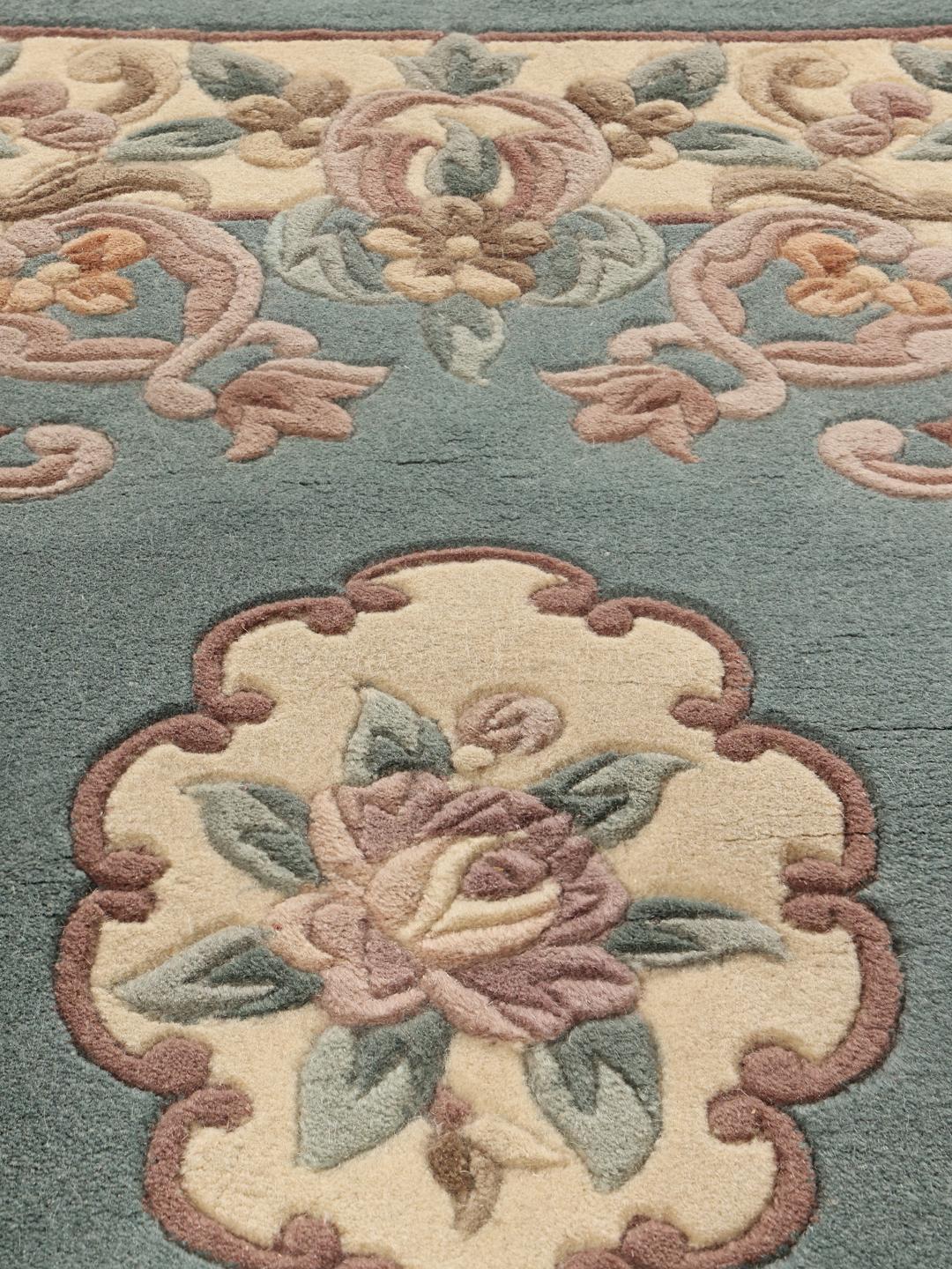 Et rektangulært håndknyttet tæppe fra Kina med et blomstermønster i lyseblå og beige.