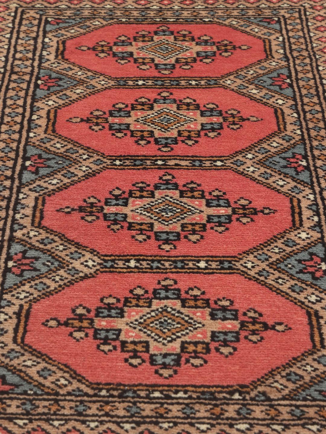 A hand-knotted Pakistan Bokhara rug with a red field and traditional medallion patterns.