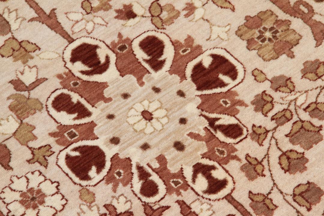 Et stort rektangulært håndknyttet tæppe fra Indien med et indviklet blomstermønster i beige og bløde røde toner.
