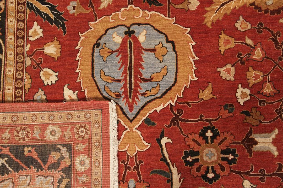 Una gran alfombra rectangular anudada a mano con un patrón tradicional floral y de medallón en rojo y negro, originaria de la India.